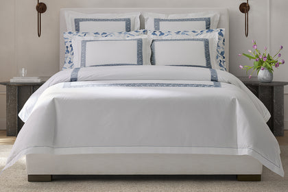 White Ophelia bedding with a blue embroidered border, styled on a bed.
