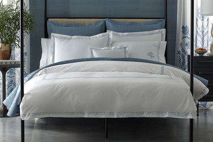White Prado bedding with a blue embroidered border, styled on a bed.