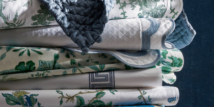 Schumacher bedding in assorted prints, stacked.