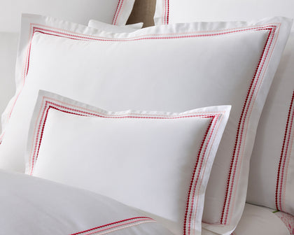 White Amara pillows with a red embroidered border, close-up.