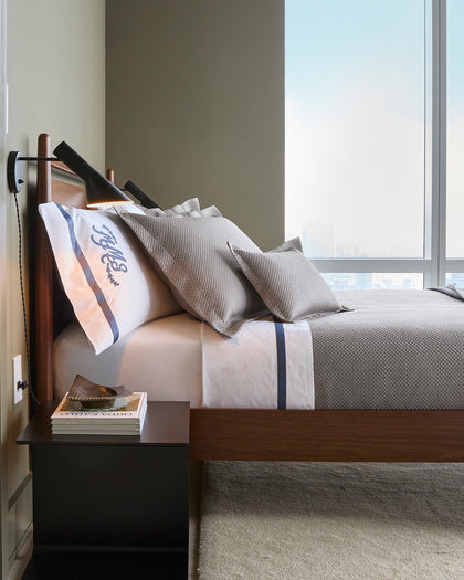 White Alba bedding with a navy stripe trim, layered with textured gray pique pillows and a throw.