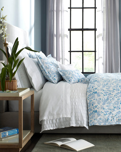 Blue Alexandra floral print bedding layered with white sheets on a bed.