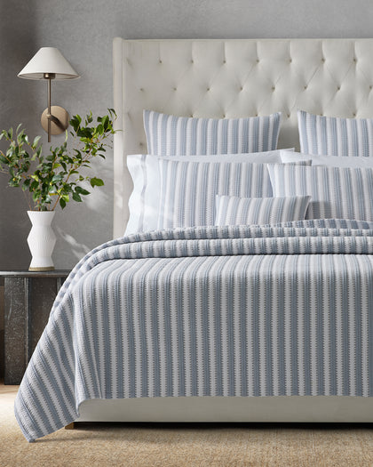 Blue and white Apollo Stripe Matelasse quilted bedding, styled against a headboard.