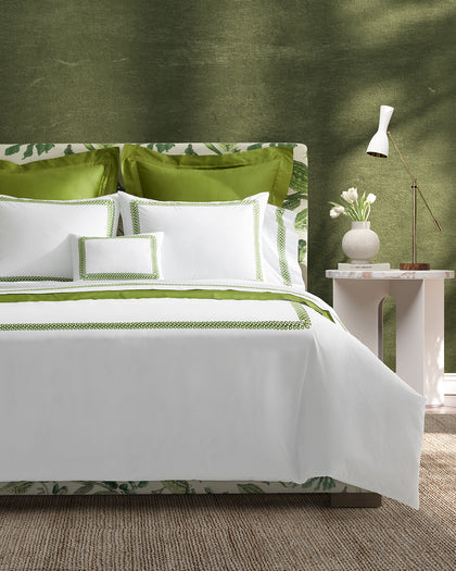 White Astor Braid sheets with green loop-embroidered trim, styled against a headboard.