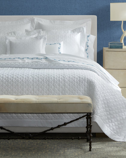 White Ava quatrefoil-quilted bedding with blue floral vine embroidery.