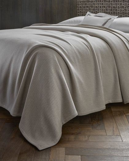 Tan Avalon herringbone-woven blanket draped over a bed.