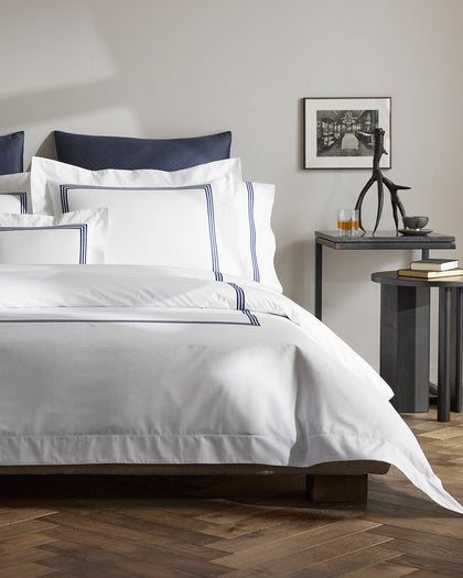 White Bel Tempo sheets with navy triple-stripe trim and a navy quilted headboard pillow.