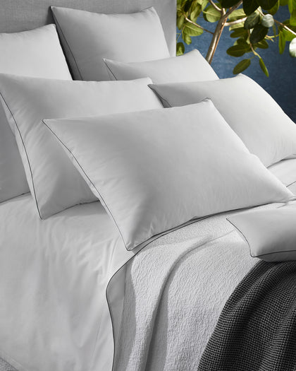White Bryant sheets with black piped trim, layered with a textured bouclé throw and a knit blanket.