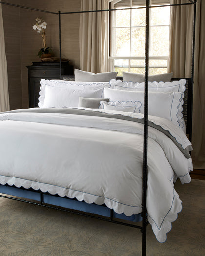 White Butterfield scalloped bedding with blue trim, styled on a bed.