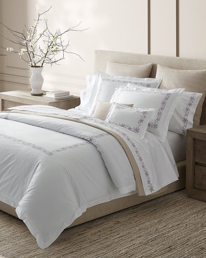 White Callista sheets with gray floral vine embroidery, styled on a bed beside flowering branches.