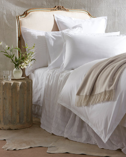 White Ceylon Satin Stitch bedding with a textured pintuck sham and tan throw, styled against a headboard.