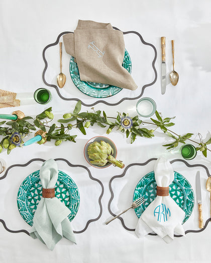 White Chamant scalloped placemats with a charcoal wavy trim, set with monogrammed linen napkins from above.