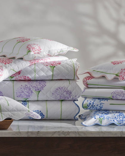 Charlotte allium-print quilted bedding stacked in pink, purple, and blue on a table.