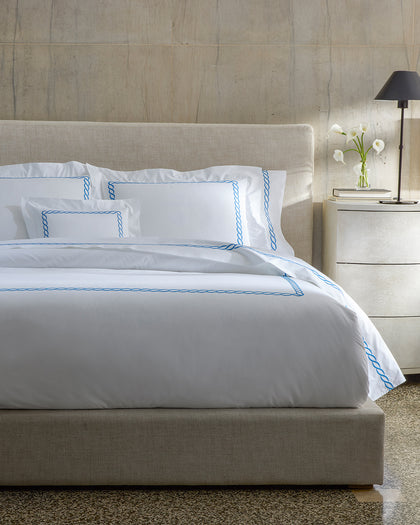 White Classic Chain sheets with blue chain-link embroidered trim, styled beside calla lilies.