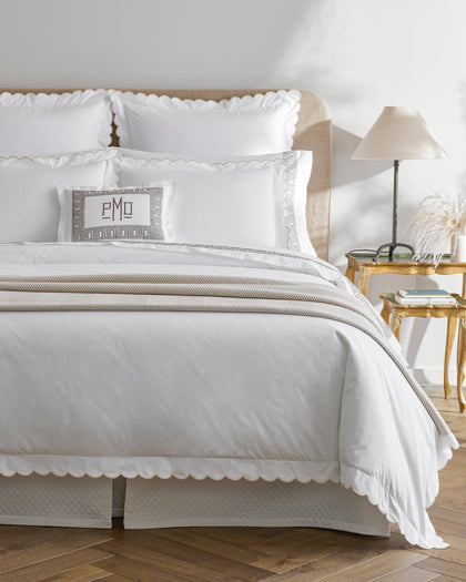 White Dakota scalloped sheets with a Greek key monogrammed pillow, styled on a bed.
