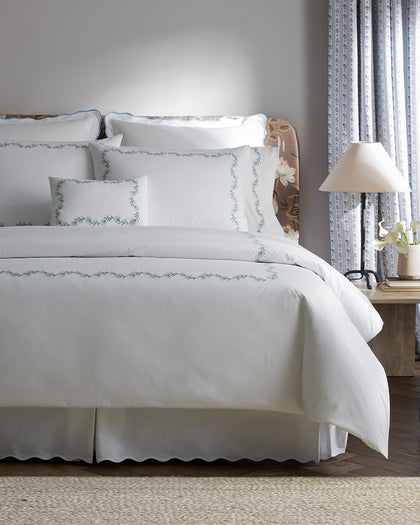 White Daphne sheets with embroidered floral trim, styled against a headboard.