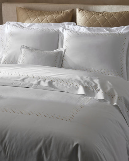 White Dorothy sheets with gold polka-dot embroidery, layered with gold quilted diamond pillows.