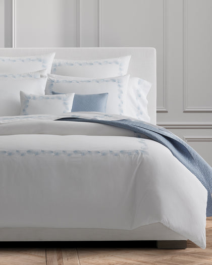 White Feather bedding embroidered with light blue feather motifs, layered with a blue quilted throw.