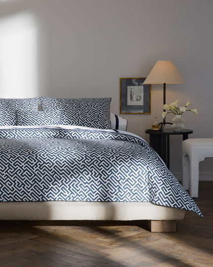 Navy Gabriel fretwork print bedding layered with white striped bordered sheets.