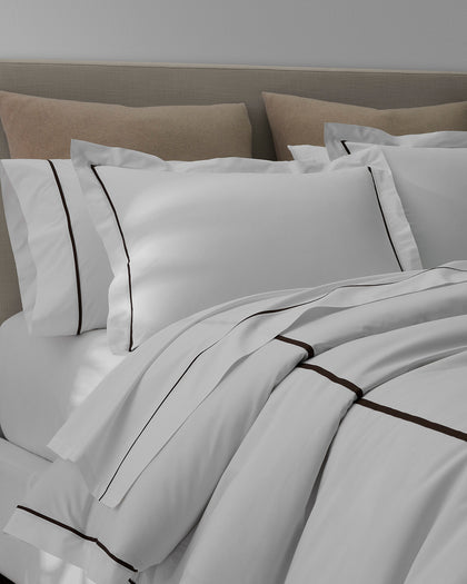 White Gatsby bedding with brown contrast piping, layered with tan pillows.