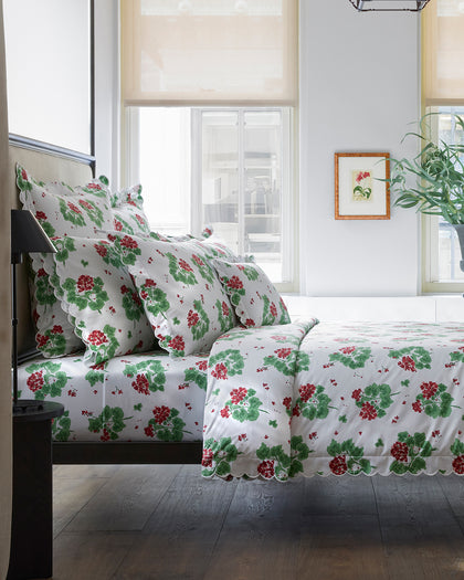 Red and green Geranium print scalloped bedding styled on a bed.