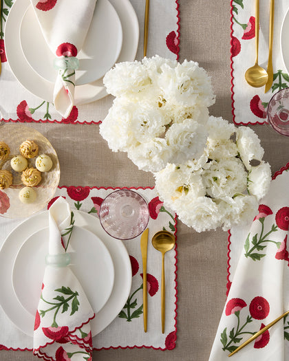 White Gisele placemats and napkins embroidered with red poppies, set with gold flatware and white carnations.