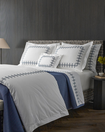 White Gordian Knot bedding with a navy embroidered knot border, layered with a navy quilted throw.