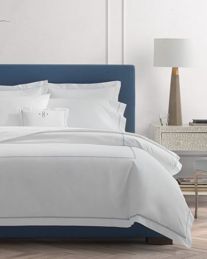 White Hatch monogrammed sheets with cross-stitch trim, styled on a bed.