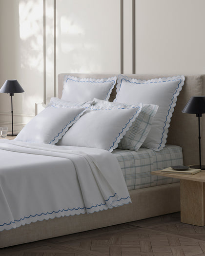 White India Pique scalloped sheets with blue trim, layered over a plaid fitted sheet.