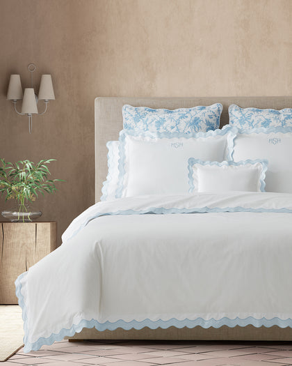 White Lorelei scalloped sheets with blue trim and monogrammed pillows, layered with blue floral toile shams.