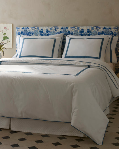White Louise sheets with a blue bordered trim, styled against a headboard.