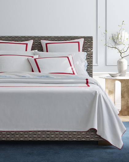 White Louise Pique sheets with a red bordered trim, styled against a headboard.