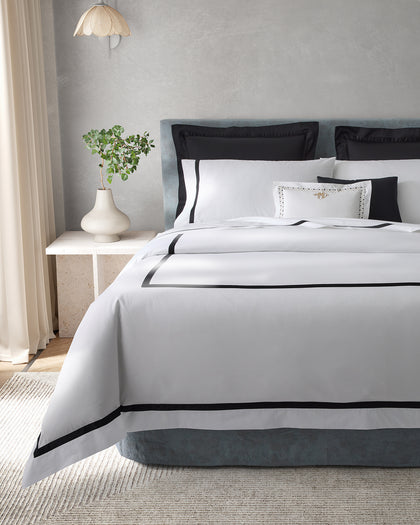 White Lowell bedding with a black ribbon trim, layered with black pillow shams on a bed.