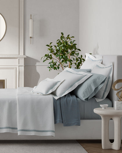 White Lowell Matelasse quilted bedding with a gray ribbon trim, styled beside a fireplace.