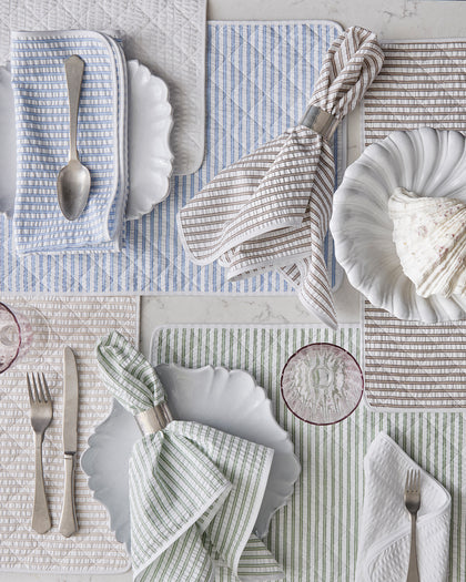 Matteo striped placemats and napkins in blue, tan, and green, set with scalloped white plates from above.