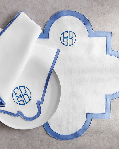 White scalloped Mirasol placemat with blue trim and monogrammed napkins.