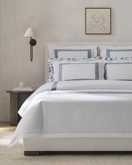 White Ophelia sheets with blue Greek key embroidered trim and a blue floral print accent pillow.