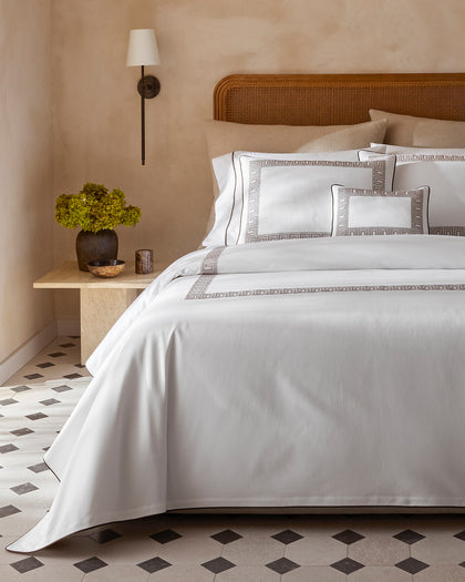 White Ophelia Pique bedding with a brown Greek key trim, styled against a headboard.