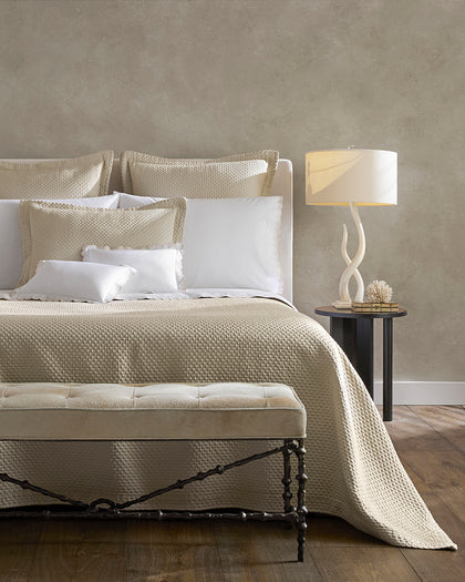 Textured cream Perla quilted bedding styled beside a bench and coral decor.