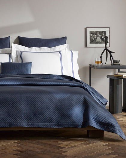 Navy diamond-quilted Petra bedding layered over white sheets with a navy triple-stripe trim.