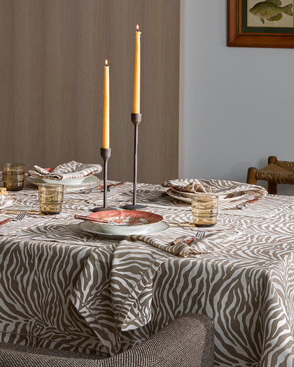 Taupe zebra-print Regine tablecloth set with candles and coral-rimmed china plates.