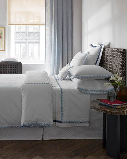 White Stella bedding with blue scalloped embroidered trim, styled against a headboard.