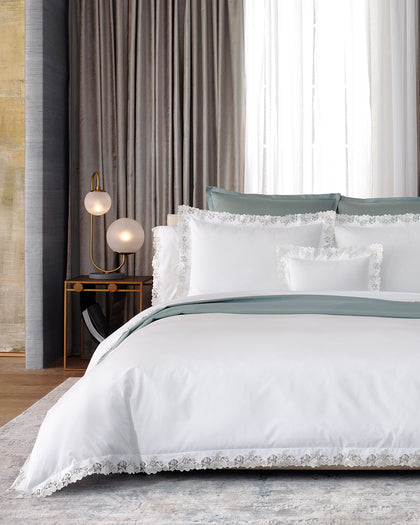 White Virginia bedding with floral lace trim, layered over sage green sheets.