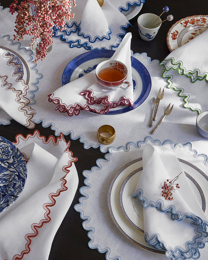 White Wave placemats and folded napkins with wavy trim in assorted colors, set with blue and white china.