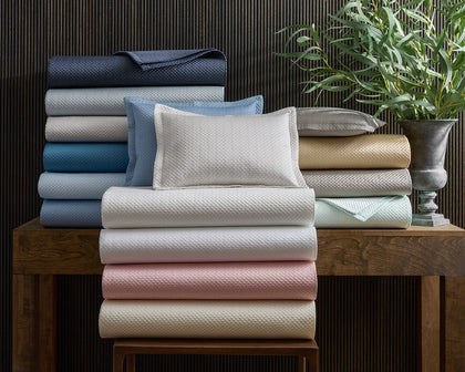 Alba textured pique bedding stacked in an array of pastel colors, near a potted plant.