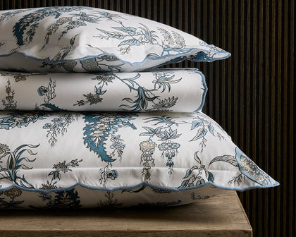 Blue Apolline floral print scalloped bedding, stacked on a wooden table.