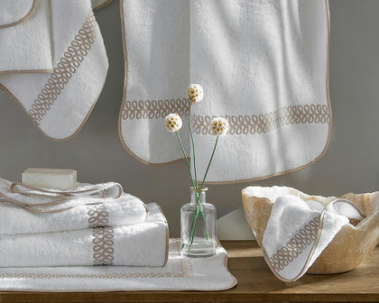 White Astor Braid towels with tan loop-embroidered trim, hung and stacked with a bud vase.