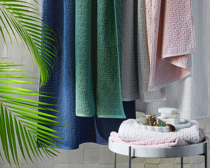 Athena greek-key textured towels in navy, green, gray, and pink, hung over a rail.