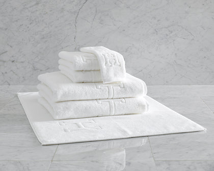 White Auberge monogrammed towels and bath mat stacked on marble tile.