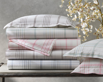 White August Plaid sheets in gray, green, pink, and blue, stacked beside cherry blossoms.